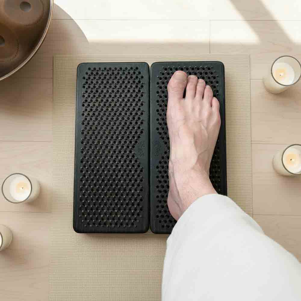 Person using a black foot massage mat with copper nails with candles and a bowl in the background