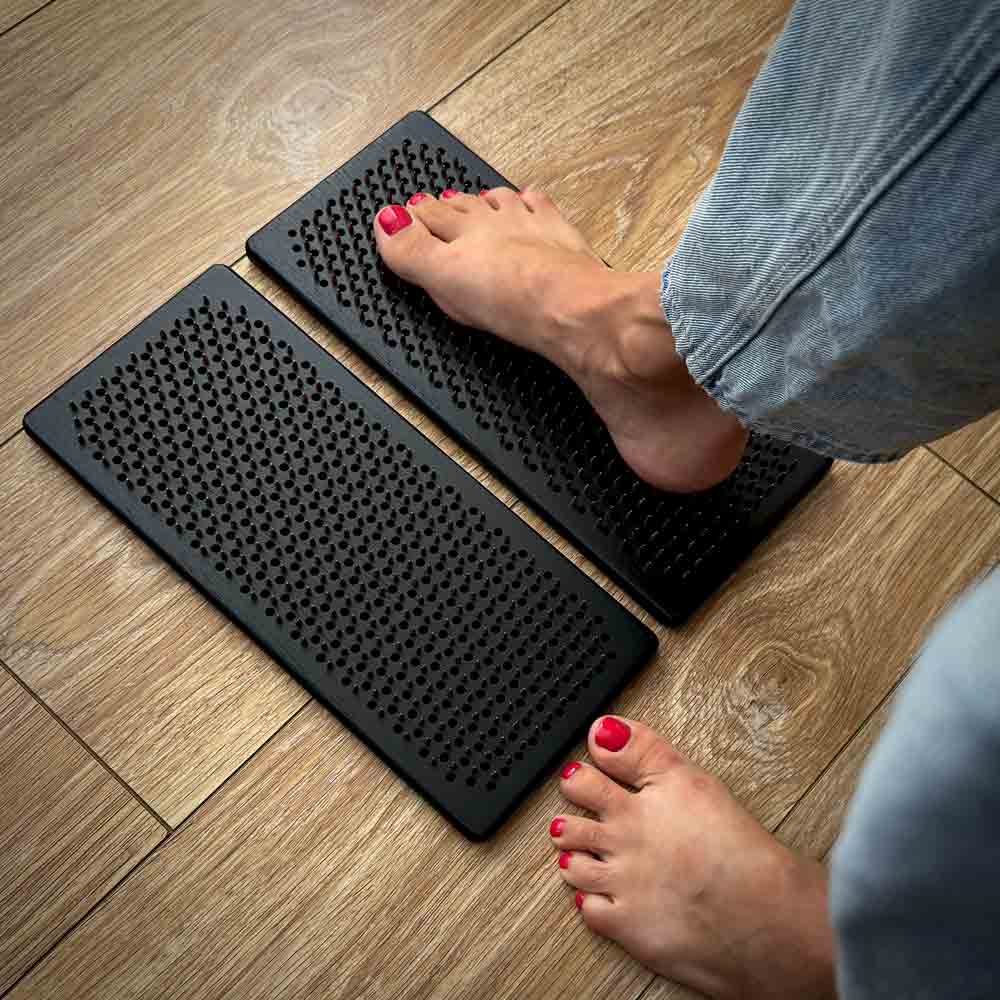 Person stepping onto a pair of black wooden sadhu boards on a wooden floor.