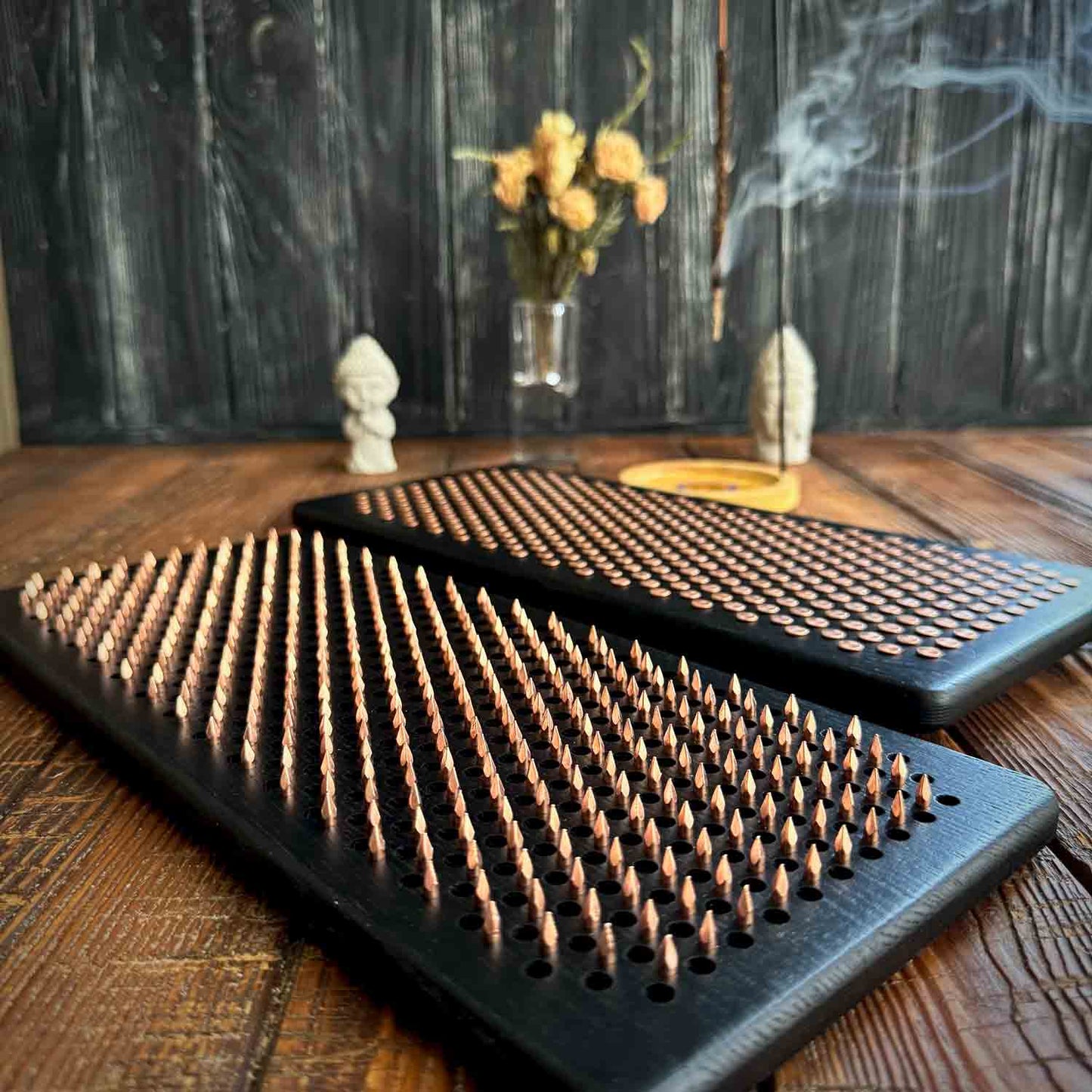 Two ash wood sadhu board with copper nails in black color, incense holders with small figurines on a dark wooden surface.
