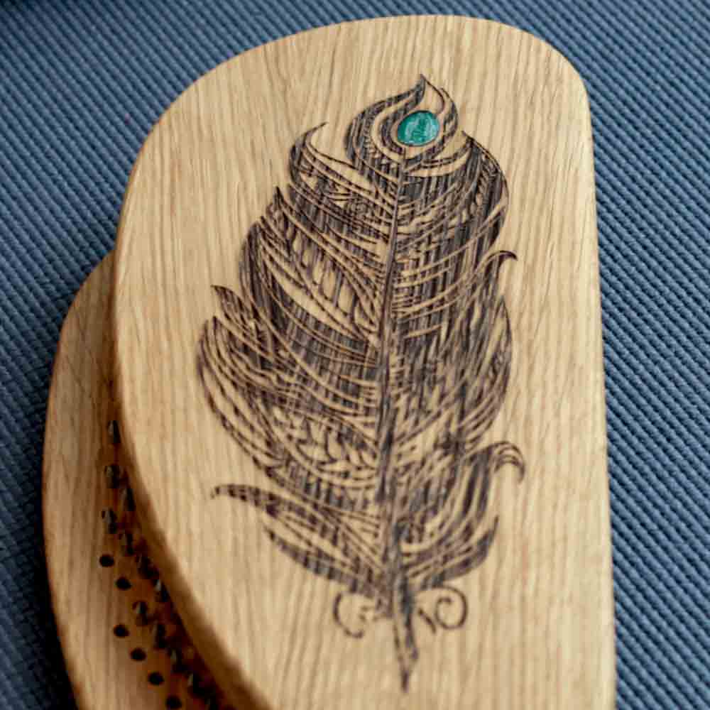 Wooden sadhu board with a engraved feather design on a blue textured background