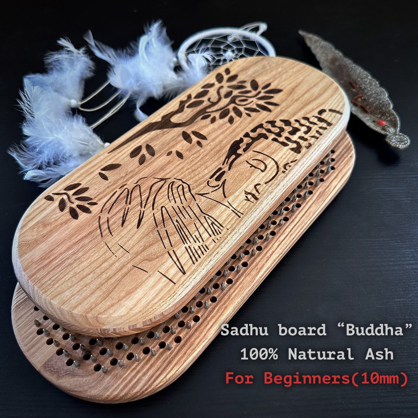 Buddha" made from 100% natural ash wood, featuring an engraved design of Buddha and a tree. The board is designed for beginners with a 10mm spacing between the holes for nails. The setup includes a dream catcher with white feathers and an incense holder, adding to the spiritual ambiance