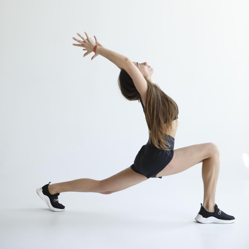 Sadhu board nails benefits for body. yoga girl in yoga pose? with hands up, right leg bend in knee in front, left leg moved back.