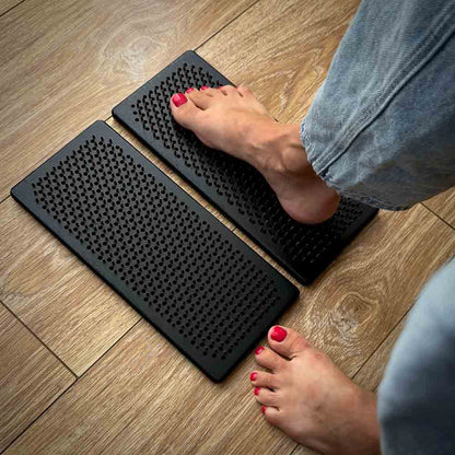 Person stepping onto a pair of black wooden sadhu boards on a wooden floor.