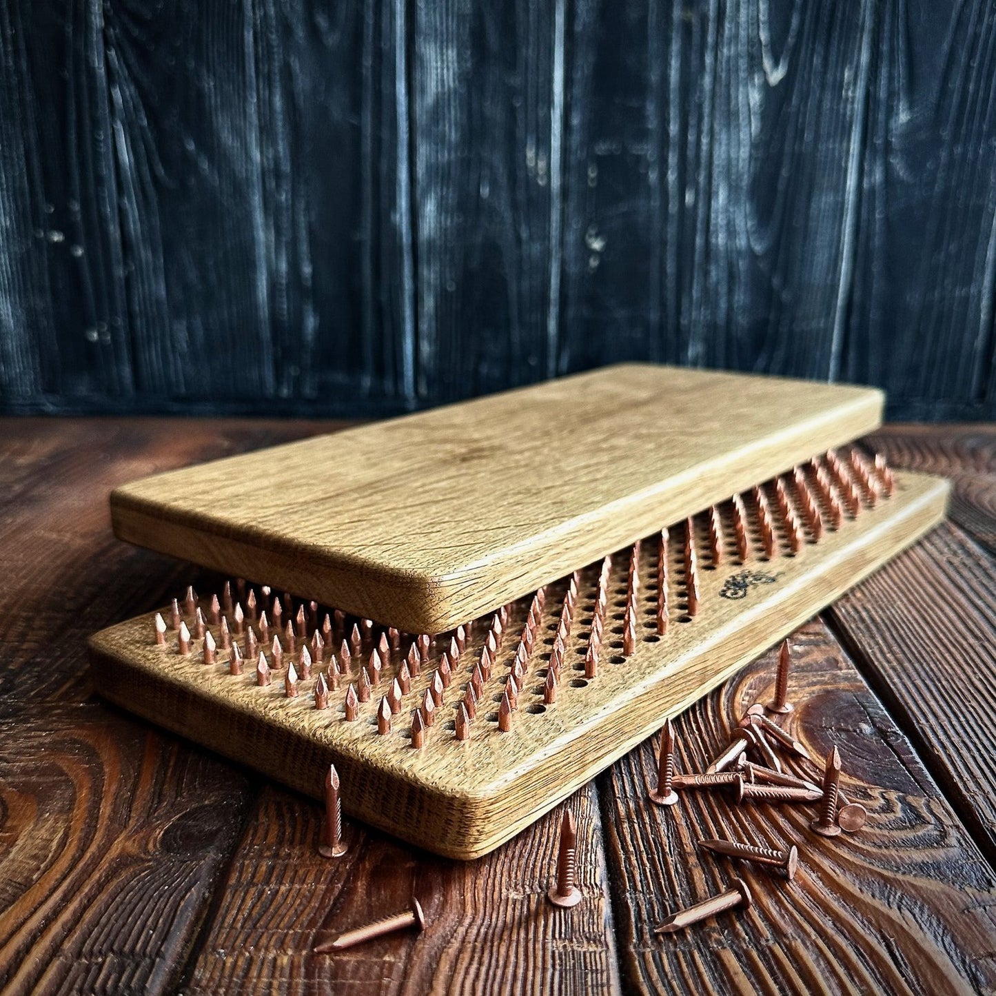 Close-up of a handcrafted Sadhu Board made from natural oak wood with copper nails. The board features a smooth, polished finish, showcasing the high-quality materials and attention to detail in its design. Several loose copper nails are scattered around, adding to the rustic and artisanal look of the product. The background is a dark wooden texture, enhancing the natural and elegant appearance of the Sadhu Board.