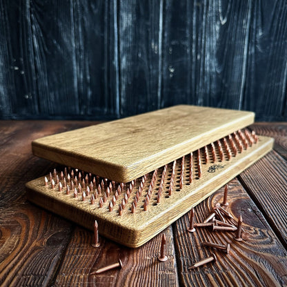 Close-up of a handcrafted Sadhu Board made from natural oak wood with copper nails. The board features a smooth, polished finish, showcasing the high-quality materials and attention to detail in its design. Several loose copper nails are scattered around, adding to the rustic and artisanal look of the product. The background is a dark wooden texture, enhancing the natural and elegant appearance of the Sadhu Board.