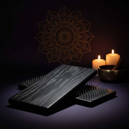 Black wood sadhu board nails on a dark surface with candles and decorative wall art in the background in yoga studio