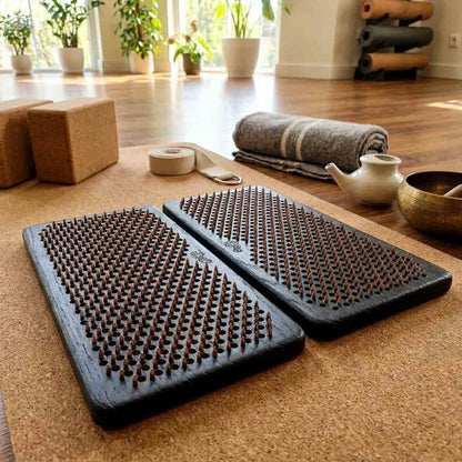 Two acupressure mats on a wooden floor with yoga props in the background.