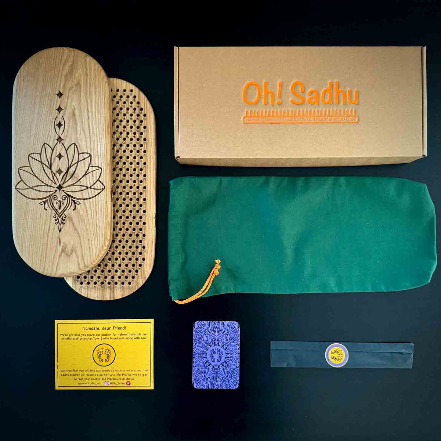 Collection of items including a wooden sadhu board with a lotus design, a box labeled 'Oh! Sadhu', a green pouch, and other accessories on a dark background.